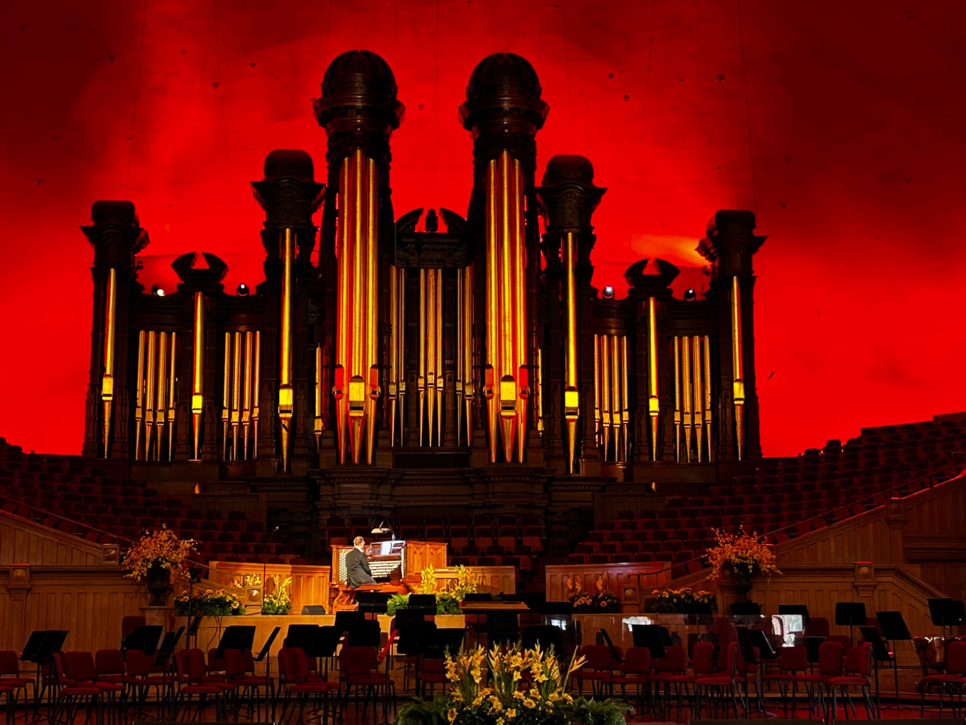 The Salt Lake Tabernacle organ lit in red, with an organist at the console and rows of chairs in the hall