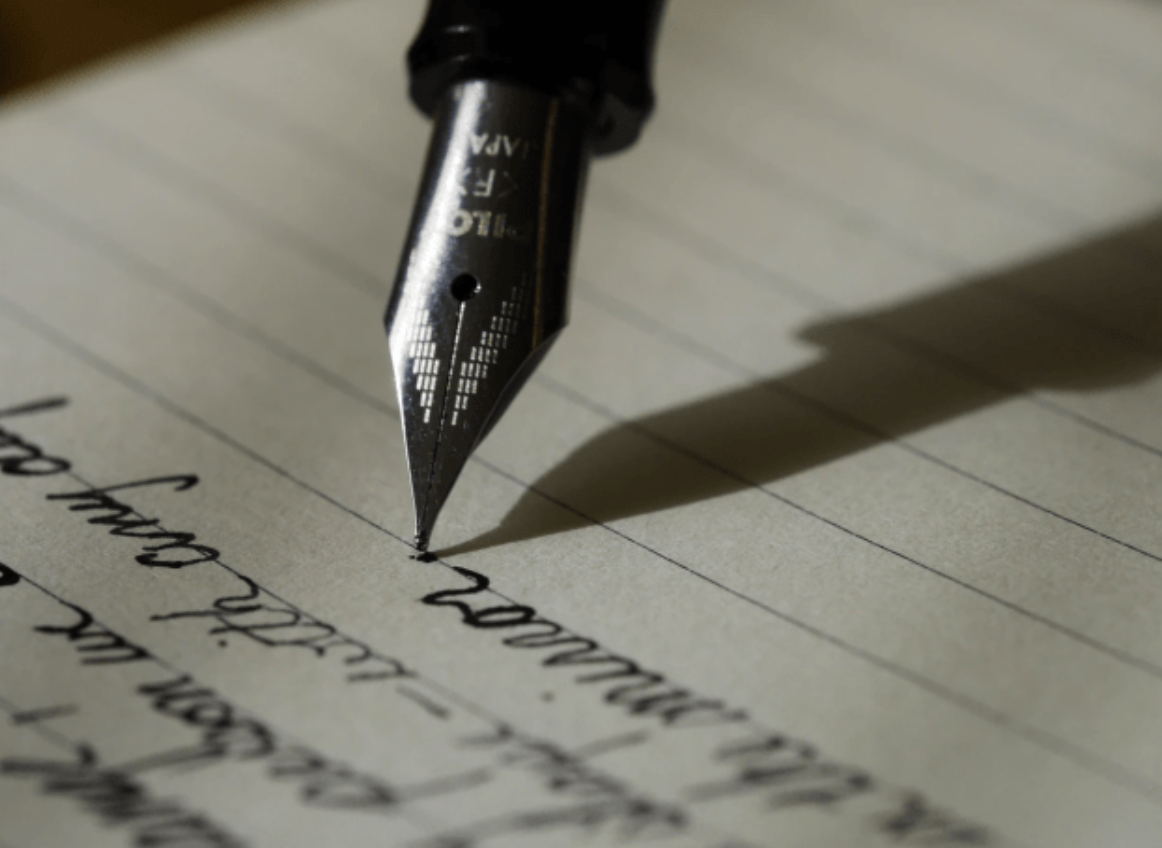 A fountain pen nib writing a letter by hand on lined paper